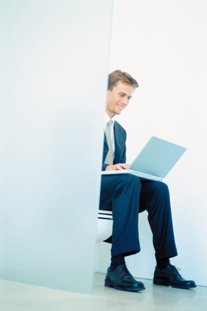 Businessman seated on toilet with laptop computerの写真素材