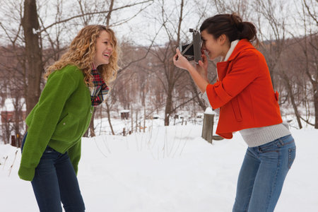 Teenage girl taking photograph of friend in snow