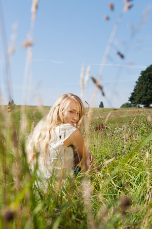 Young woman sitting in a field, smiling backwards at the cameraの写真素材