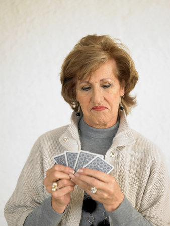 Senior woman playing cards pulling faceの写真素材