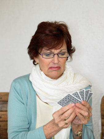 Senior woman playing cards pulling faceの写真素材