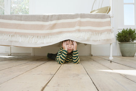 Boy hiding under a bedの写真素材
