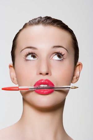 Young woman with pen in her mouthの写真素材