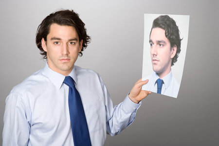 Portrait of a man holding a photograph of himselfの写真素材