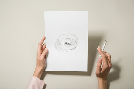 A woman holding a photograph of an ashtray and a cigaretteの写真素材