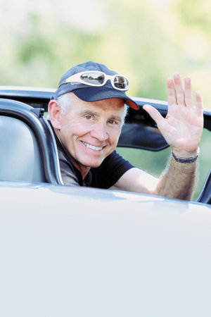 Portrait of a senior man waving in his convertible