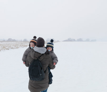 Woman Walking With Twin Sons In Snowの写真素材