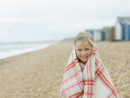 Young Girl Huddled In Blanket On Beachの写真素材