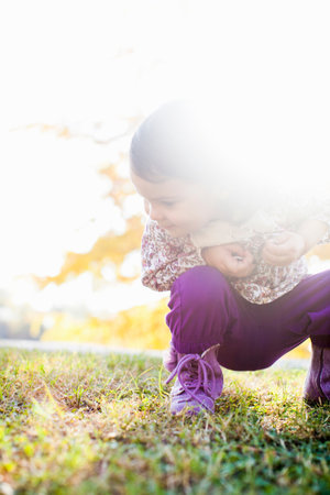 Child Squatting Looking Down At Grassの写真素材