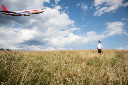 Businessman In Field Looking At Airplane