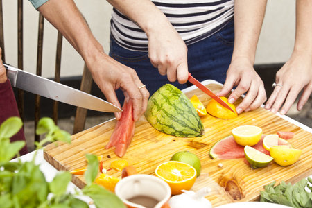 Hands Of Three Women Preparing Fresh Fruit At Garden Tableの写真素材