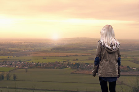 Young Woman Watching Sunrise Over Rural Landscapeの写真素材
