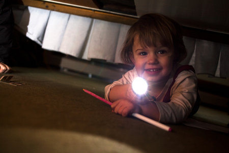 Young Girl Playing With Torch Underneath Bedの写真素材