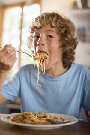 Teenage Boy Eating Spaghetti At Dining Tableの写真素材