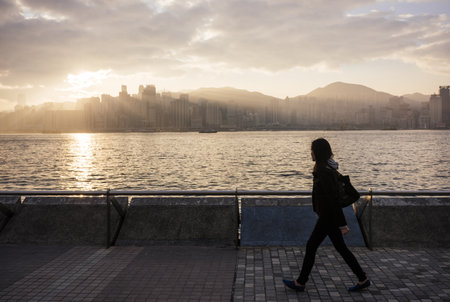 Side View Of Young Woman Walking Past Water, Hong Kong, Chinaの写真素材