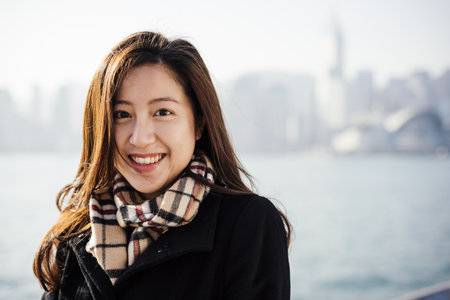 Portrait Of Young Woman Wearing Checked Scarf In Front Of Water, Looking At Camera Smilingの写真素材