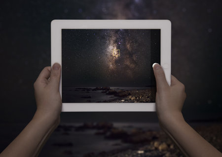 Hands Of Young Woman Holding Up Digital Tablet With View Of Milky Way In Front Of View Of Milky Way At Night, Crete, Greeceの写真素材