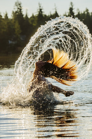 Side View Of Young Woman In Water Throwing Wet Hair Back Arms Openの写真素材