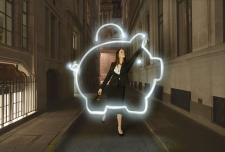 Businesswoman Light Painting Glowing Piggy Bank Symbol On City Street At Nightの写真素材