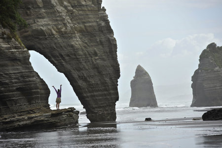 Young Woman With Arms Open On Beach Rock Formation, North Island, New Zealandの写真素材