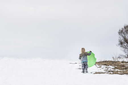 Rear View Of Child Carrying Toboggan In Snow
