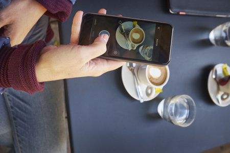 Overhead View Of Mid Adult Woman Photographing Table On Smartphone At Sidewalk Cafe