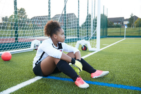 UK, Tired female soccer goalie (12-13) sitting at goalの写真素材