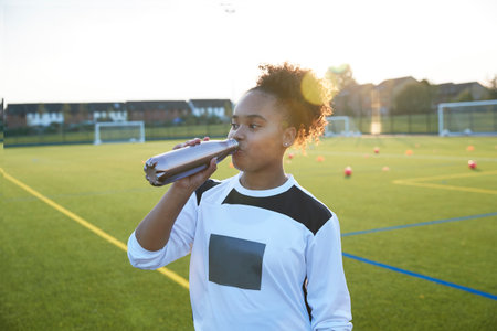 UK, Female soccer player (12-13) drinking from bottle in fieldの写真素材