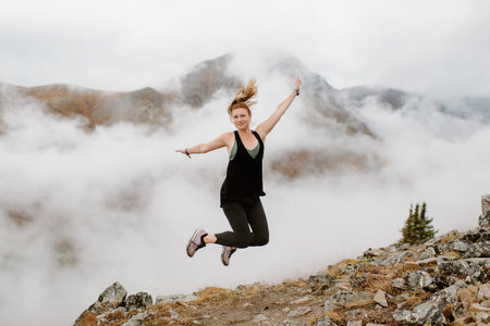Canada, Whitehorse, Woman jumping fog covered mountain landscapeの写真素材