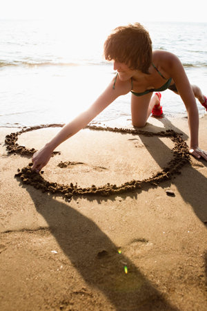 Woman drawing heart in sand on beachの写真素材