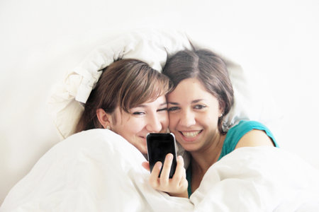 Teenage girls using cell phone in bedの写真素材