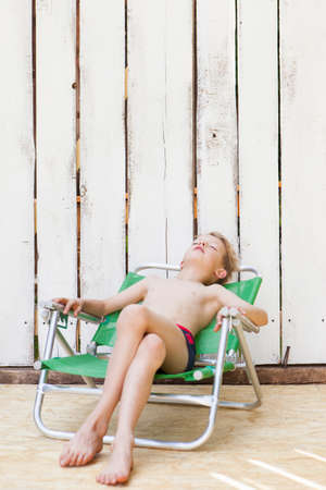 Boy in swimsuit in lawn chair indoorsの写真素材