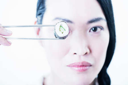 Woman holding piece of sushi over eyeの写真素材