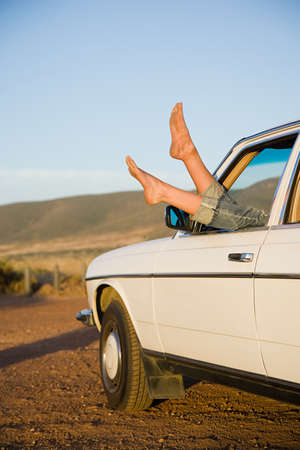 Young womans feet sticking out of a car windowの写真素材