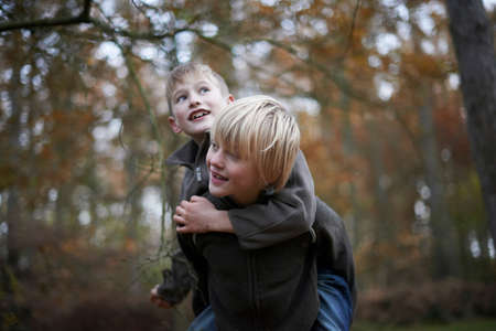 Boy giving friend a piggyback through forestの写真素材