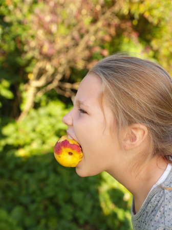 Young girl holding peach in mouth, profileの写真素材