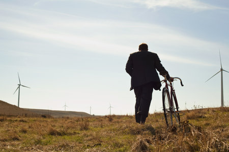 Man pulling bicycle uphill towards windfarmの写真素材