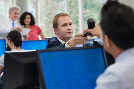 Office worker passing telephone to colleague in office