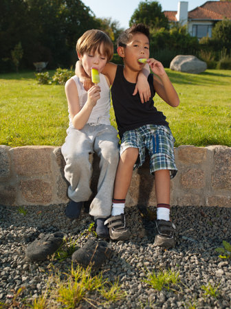 Boys sitting on wall and enjoying ice loliies, portraitの写真素材