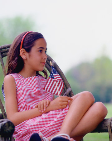 Girl sitting on porch holding US flagの写真素材