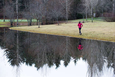 Woman running by still rural lakeの写真素材