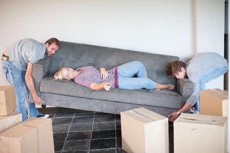 Young woman moving house on sofa being carried by menの写真素材