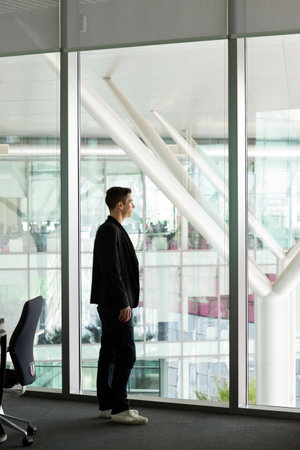 Young man looking out of window in IT officeの写真素材