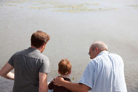 Boy at river with father and grandfatherの写真素材