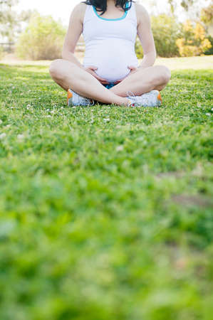 Pregnant young woman sitting cross legged on grassの写真素材