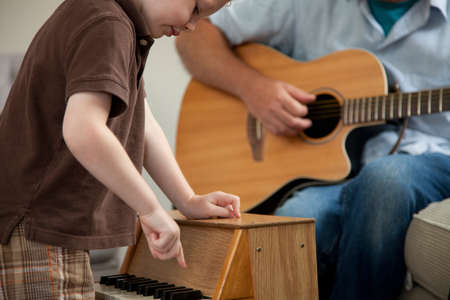 Boy playing little piano as man plays guitarの写真素材