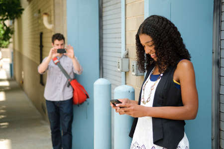 Man photographing girlfriend as she looks at cellphone