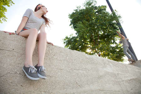 Young woman sitting on wall watching skateboarderの写真素材
