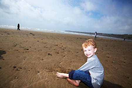 Boy sitting on beach smilingの写真素材