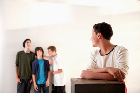 Teenage boy leaning on box with friends in backgroundの写真素材